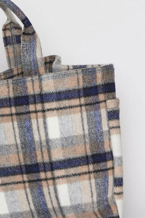 A close-up image of the PLAID TOTE by Velvet by Graham & Spencer showcases its plaid-patterned fabric in shades of blue, gray, white, and beige. The tote bag features dual handles and has a soft texture.