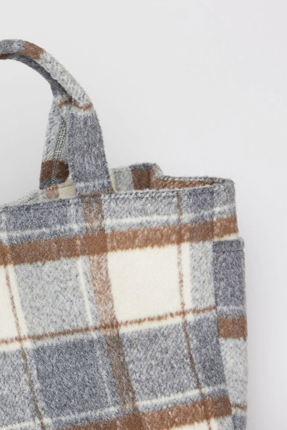   Close-up of the PLAID TOTE by Velvet by Graham & Spencer, showcasing its plaid pattern in shades of gray, brown, and beige. The handle is positioned on the top left of the image. 