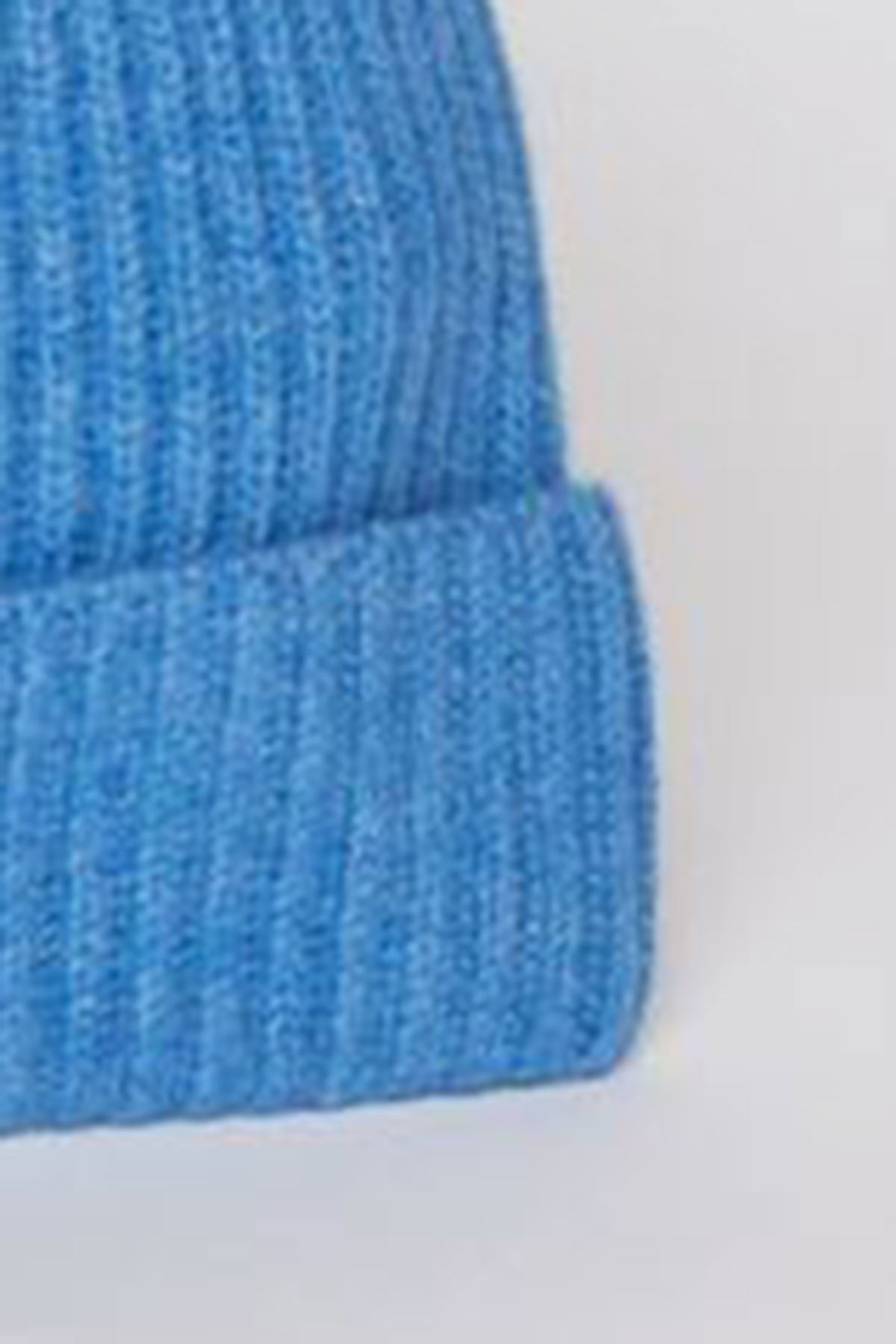   Close-up image of the Velvet by Graham & Spencer CASHMERE RIB BEANIE, a blue knitted beanie hat featuring a fold-over brim. 