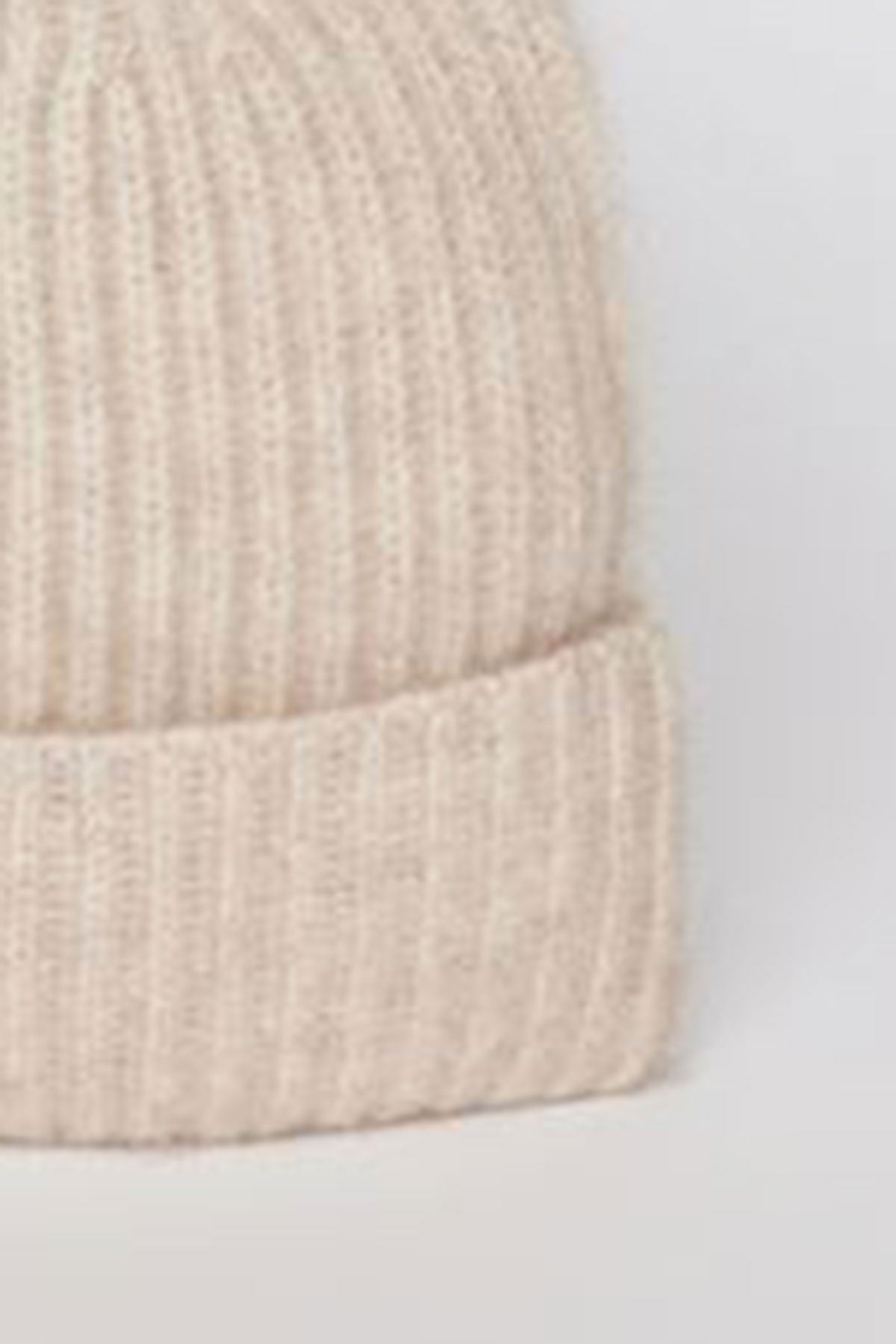   Close-up view of the CASHMERE RIB BEANIE by Velvet by Graham & Spencer, showcasing its beige knit design with ribbed texture and folded brim against a neutral background. 