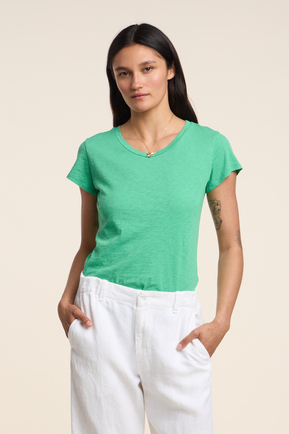 A person models the ODELIA TEE by Velvet by Graham & Spencer—a green cotton slub crewneck—paired with white pants and hands in pockets, highlighting this must-have wardrobe essential against a plain background.-41527104700609