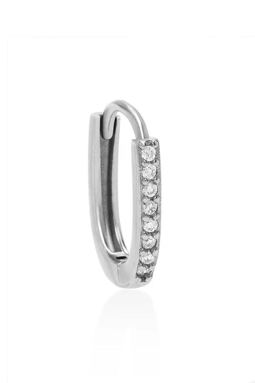 Close-up of a silver oval huggie earring showcasing a row of small round diamonds on the front against a white background