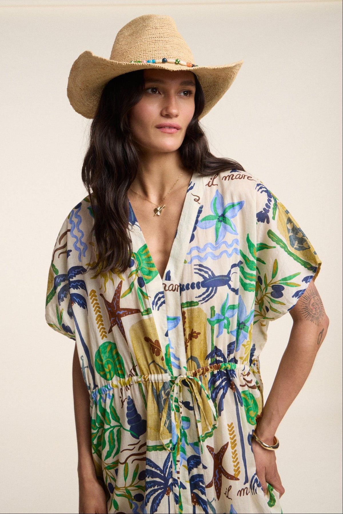 A person wearing Velvet by Graham & Spencer’s PIPPA DRESS, a colorful ocean-themed cotton voile kaftan, and a straw hat stands against a plain background.-41527443652801