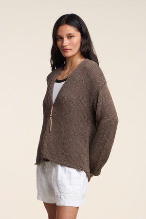 A woman wears the QUINNLY CARDIGAN by Velvet by Graham & Spencer—an open-front cotton tape yarn style—over a white top and shorts, standing against a plain light background.