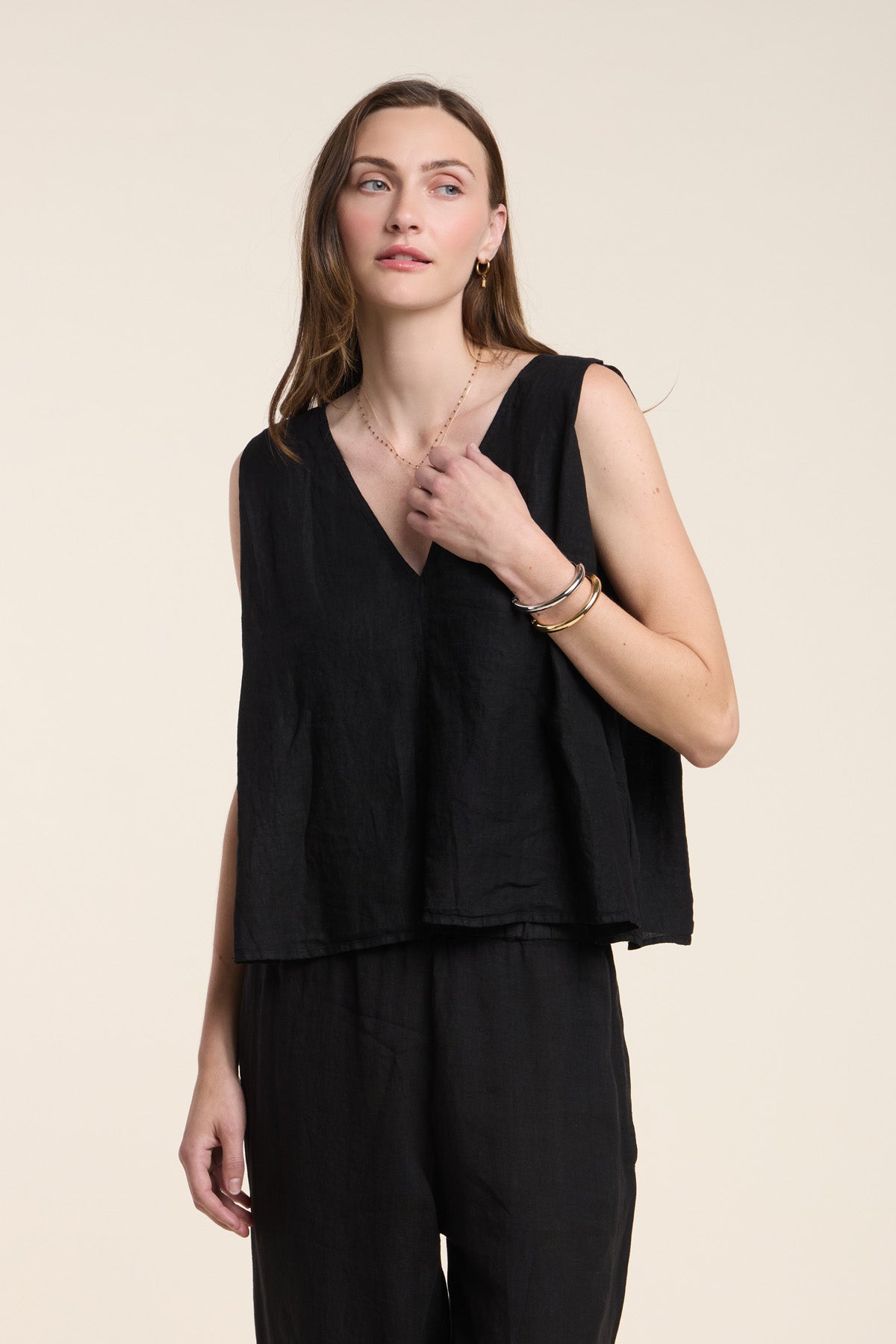A woman wears the RENNA LINEN TOP by Velvet by Graham & Spencer—a sleeveless, V-neck summer top—paired with black pants, standing against a plain light background.