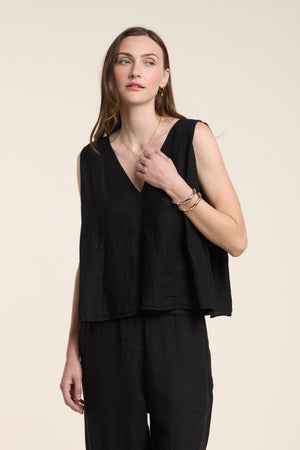 A woman wears the RENNA LINEN TOP by Velvet by Graham & Spencer—a sleeveless, V-neck summer top—paired with black pants, standing against a plain light background.