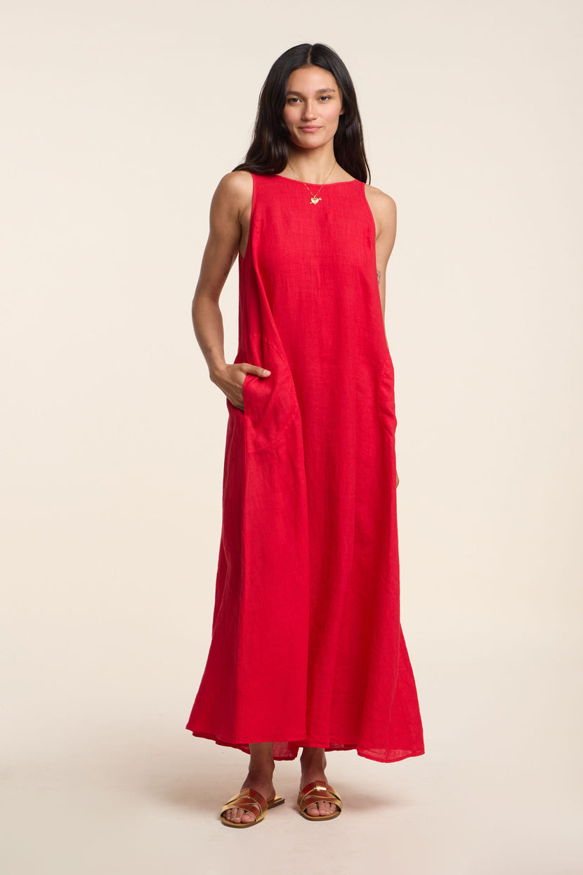 A woman poses against a plain light background in the RETA LINEN DRESS by Velvet by Graham & Spencer—a sleeveless, ankle-length maxi with side pockets, styled with flat sandals and a necklace for effortless warm-weather dressing.