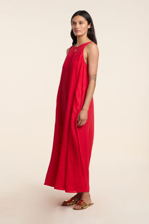 A woman wears the Velvet by Graham & Spencer RETA LINEN DRESS and gold sandals, standing against a plain, light background—an ideal look for warm-weather days.