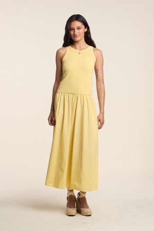 A woman faces forward in the ROMILLY DRESS by Velvet by Graham & Spencer, a sleeveless yellow cotton poplin dress paired with wedge sandals, set against a plain light background.