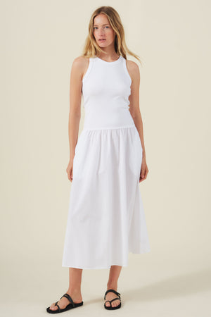 A woman stands against a neutral background wearing the ROMILLY DRESS by Velvet by Graham & Spencer, a sleeveless white midi dress with a fitted ribbed bodice, paired with black sandals.