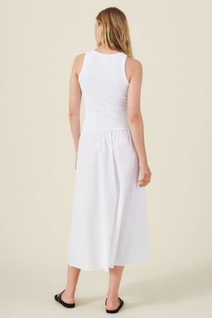 A woman stands facing away, wearing the ROMILLY DRESS by Velvet by Graham & Spencer, a cotton poplin style with a fitted ribbed bodice, paired with black sandals against a plain light background.