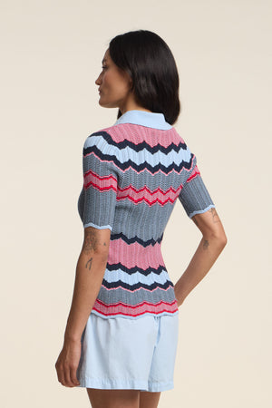 A woman faces away, wearing the Velvet by Graham & Spencer ROSELLE POLO with red, blue, and white zigzag stripes and a fitted silhouette, paired with light blue shorts.