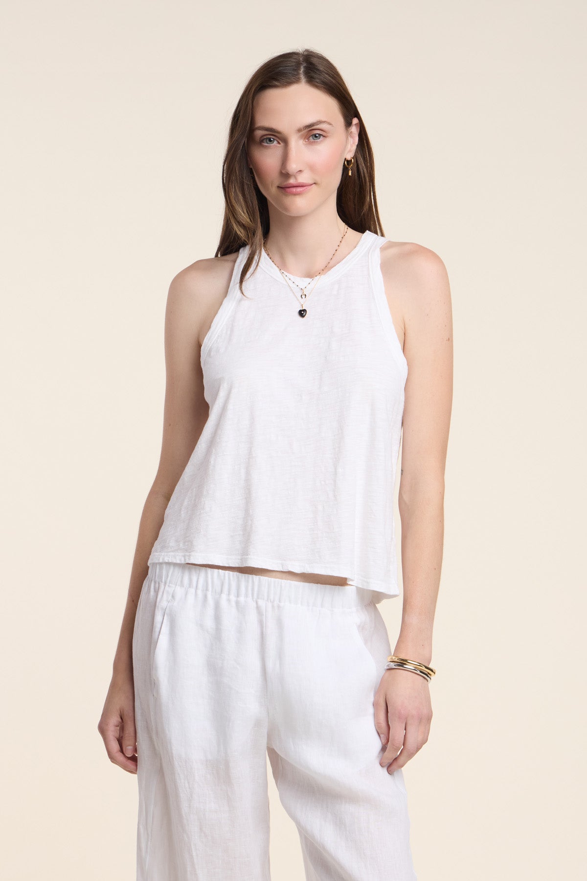 A woman stands facing the camera against a plain light background, wearing the SASHA TANK TOP by Velvet by Graham & Spencer and white pants.-41645104693441
