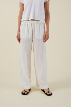 A person wears a white short-sleeve shirt, Velvet by Graham & Spencer's STEPHANIE LINEN PANT with an elastic waist, and black sandals, standing against a plain beige background.