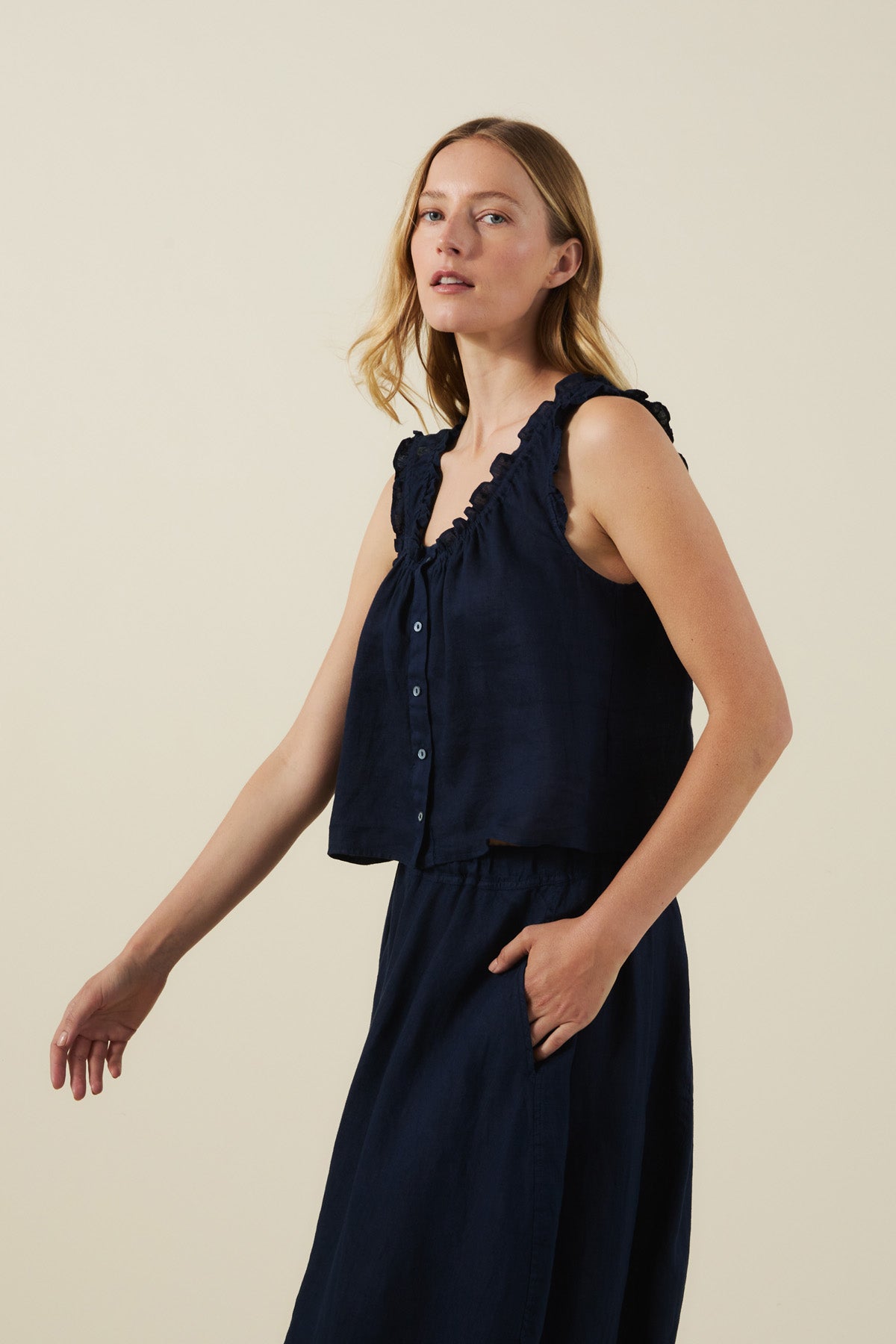 A woman models the TANA LINEN TOP by Velvet by Graham & Spencer—a sleeveless, button-front linen top—paired with a matching skirt against a plain beige background.