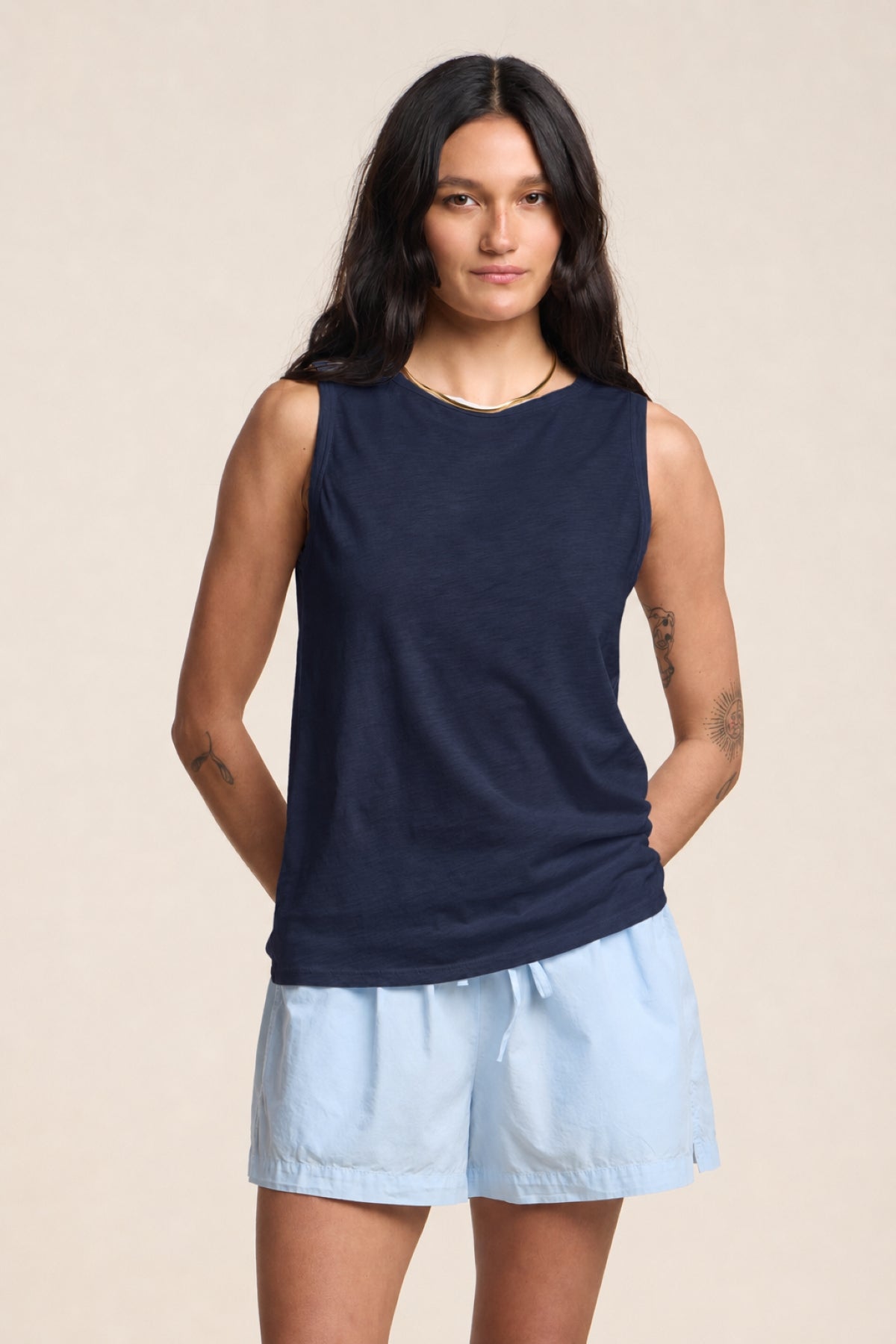 A person models the TAURUS TANK TOP by Velvet by Graham & Spencer, a sleeveless navy crew neck essential for any casual wardrobe, paired with light blue shorts against a plain background.