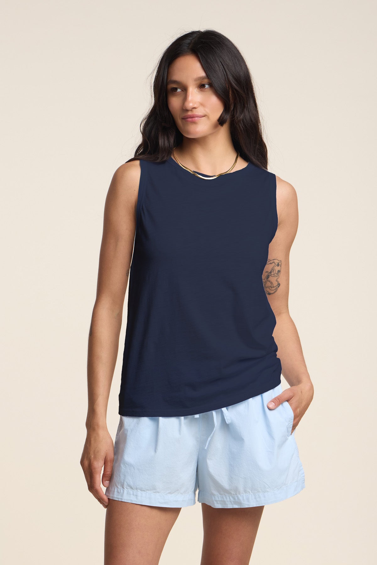 A woman with long dark hair wears the Velvet by Graham & Spencer TAURUS TANK TOP, a navy crew neck sleeveless textured cotton slub piece, paired with light blue shorts. She stands against a plain background with one hand in her pocket.-41633302937793
