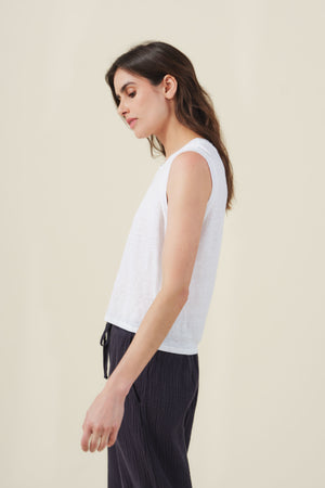 The TRINITY TANK TOP by Velvet by Graham & Spencer—a white cropped linen knit tank with a subtly sheer finish—adds a perfect layering touch when paired with dark pleated pants.