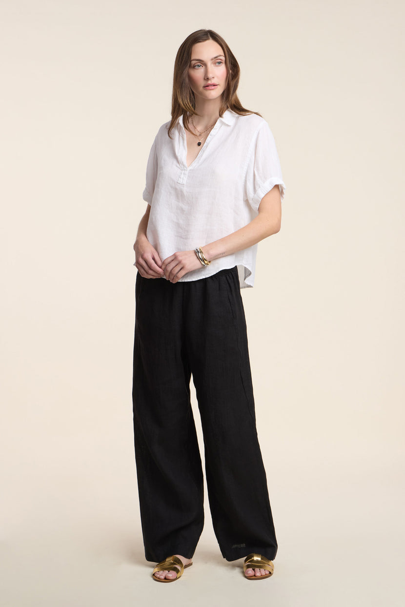 A woman faces forward wearing the VIVICA LINEN TOP by Velvet by Graham & Spencer, paired with wide black pants, gold sandals, and minimal jewelry—an easy, stylish look for warm days against a simple light background.