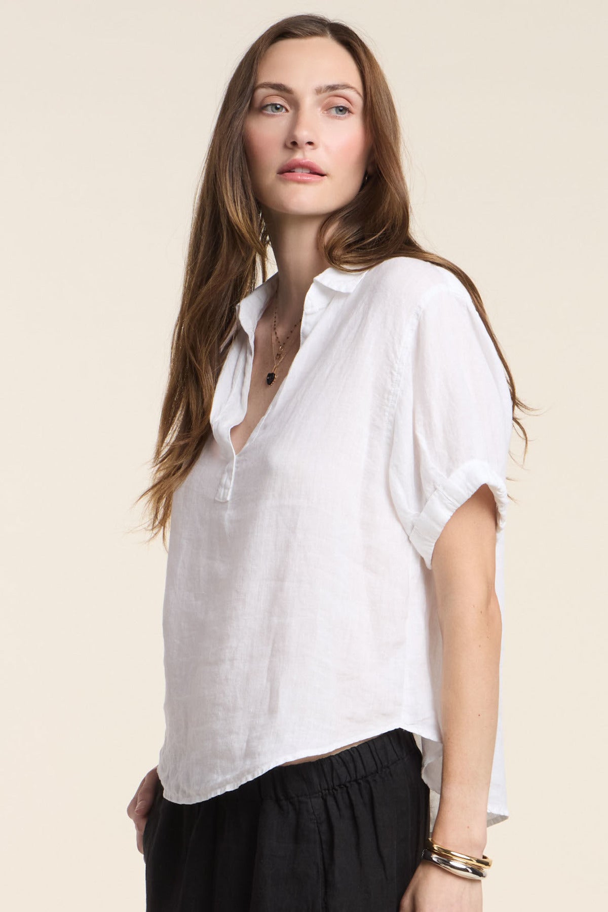 A woman with long brown hair wears the VIVICA LINEN TOP by Velvet by Graham & Spencer—a loose, woven linen top with a split neckline and short sleeves—paired with black pants, ideal for effortless warm-weather style.-41374579032257
