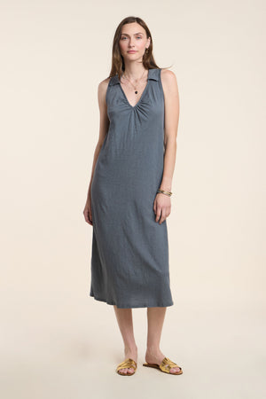 A woman stands against a plain light background wearing the Velvet by Graham & Spencer YORK DRESS, a sleeveless midi cotton slub dress with a V-neckline, paired with yellow sandals.