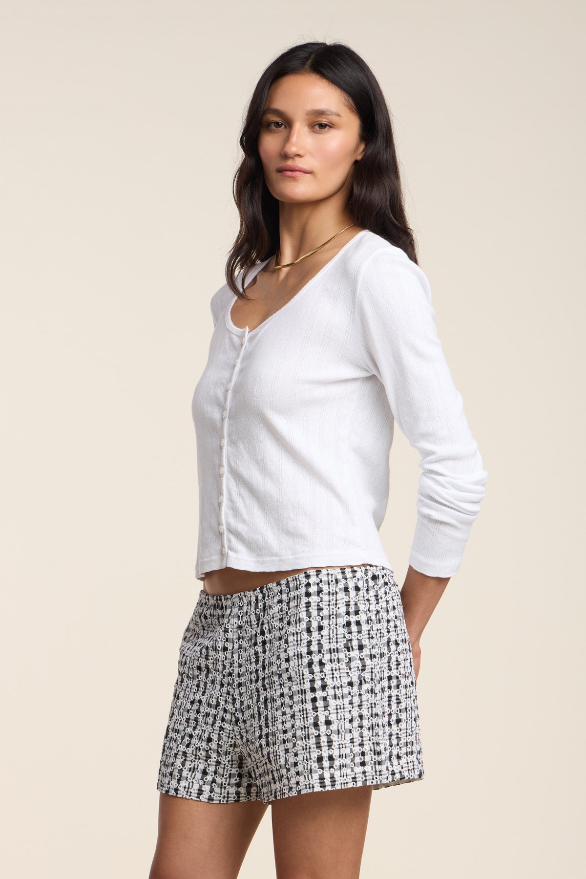 Woman standing against a plain background, wearing the ZELDA CARDIGAN by Velvet by Graham & Spencer and black-and-white patterned shorts, looking at the camera with a neutral expression.-41527126884545