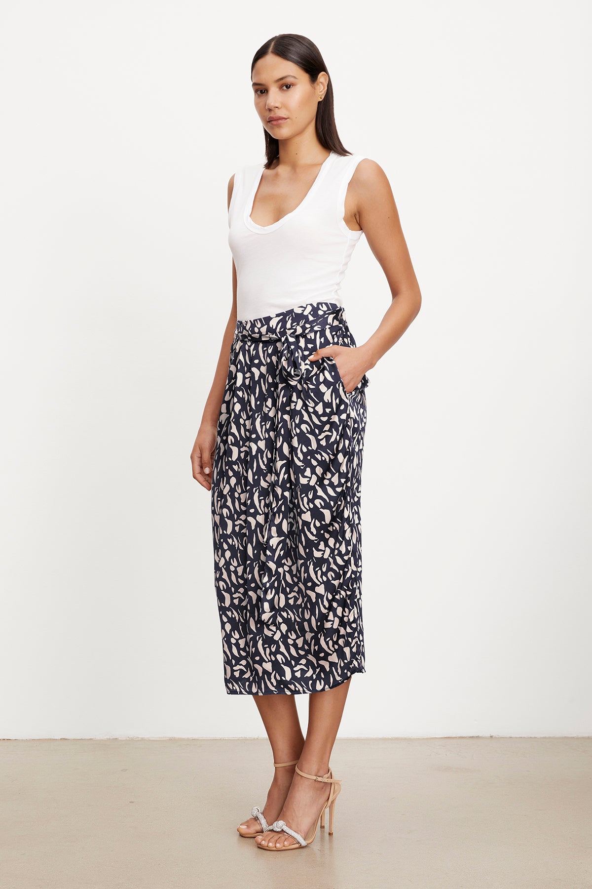   Woman modeling a white tank top with a high-waisted JUNO printed satin skirt from Velvet by Graham & Spencer and strappy heels. 