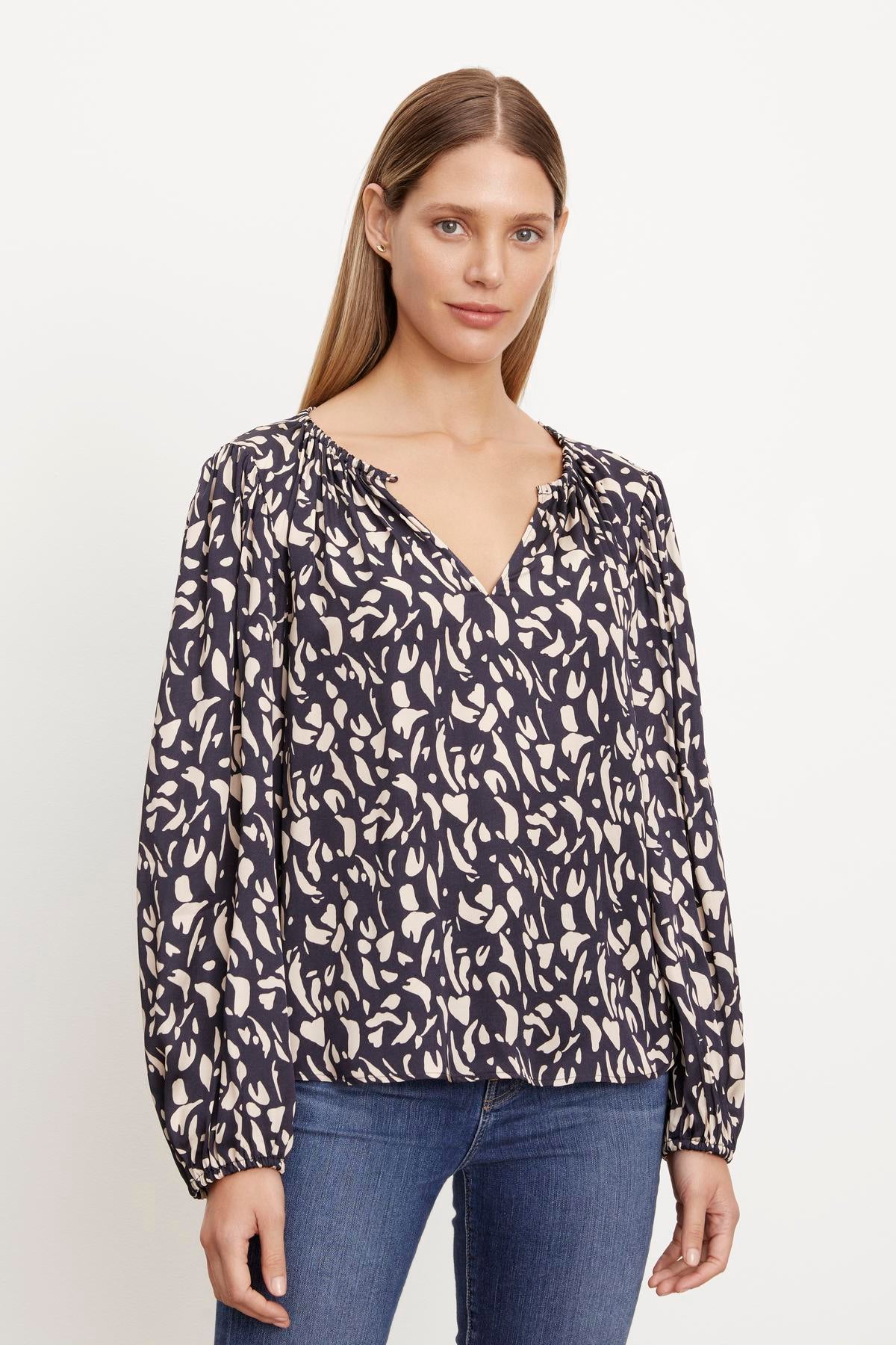 A woman wearing jeans and a KADE PRINTED PEASANT BLOUSE by Velvet by Graham & Spencer with an animal print.-36094325981377
