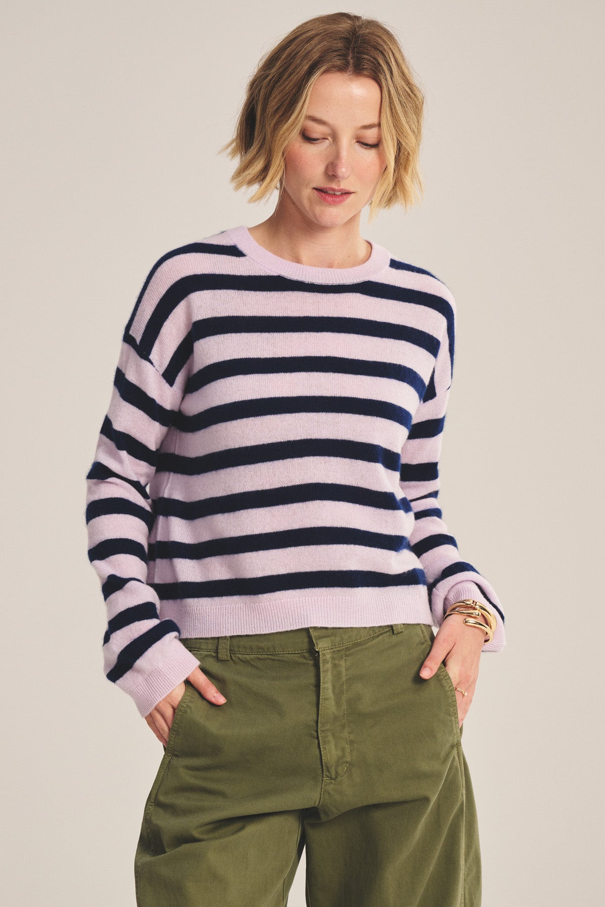 A woman models the AGNESE CASHMERE SWEATER by Velvet by Graham & Spencer—light purple and navy striped—for versatile, lightweight warmth, paired with olive green pants against a plain background.