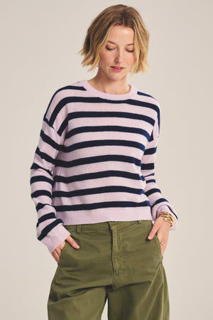 A woman models the AGNESE CASHMERE SWEATER by Velvet by Graham & Spencer—light purple and navy striped—for versatile, lightweight warmth, paired with olive green pants against a plain background.