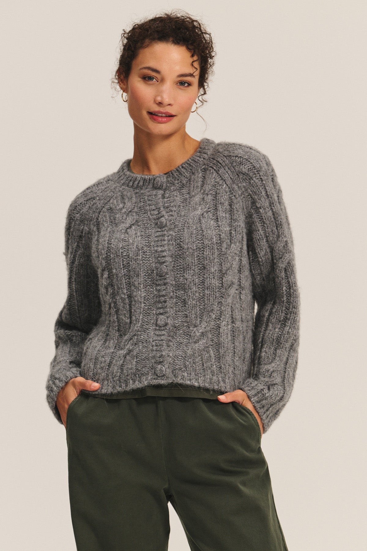 A woman wears the ALLISON CARDIGAN by Velvet by Graham & Spencer in textured gray, styled with olive green pants—an effortlessly cozy layering piece for any occasion.