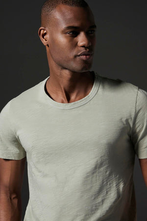 A man is shown wearing the AMARO TEE by Velvet by Graham & Spencer, looking to the side against a plain dark background, exuding a relaxed and stylish feel.