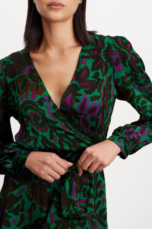 A woman wearing the Velvet by Graham & Spencer BRIDGET PRINTED SATIN WRAP DRESS with an adjustable tie waist.