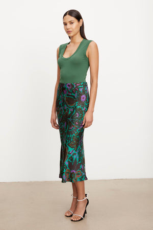 The model is wearing a green top and Velvet by Graham & Spencer's KAIYA PRINTED SKIRT with an elastic waist, creating an A-line silhouette.