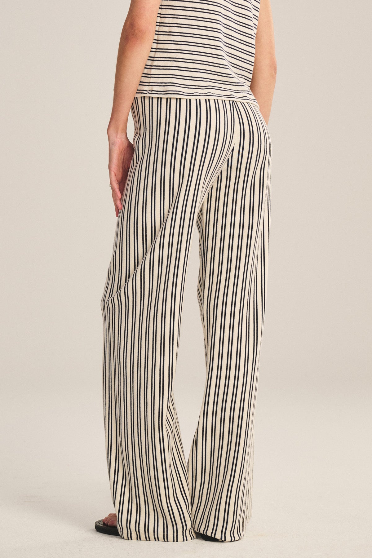 Wearing the Velvet by Graham & Spencer AMELISE SWEATPANT—relaxed, cream with black stripes and a drawstring waist—a person faces away from the camera, hand in pocket, paired with a matching sleeveless striped top.-40909622214849