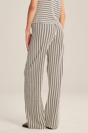 Wearing the Velvet by Graham & Spencer AMELISE SWEATPANT—relaxed, cream with black stripes and a drawstring waist—a person faces away from the camera, hand in pocket, paired with a matching sleeveless striped top.