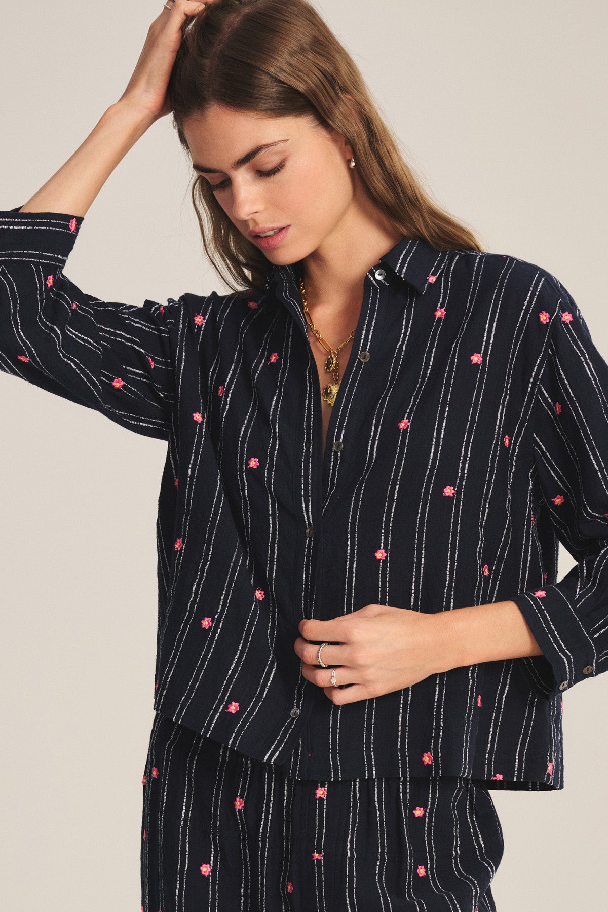 A woman wearing the ASTREN SHIRT by Velvet by Graham & Spencer: a navy blue, long-sleeve, button-up shirt with white stripes and pink floral prints, paired with matching pants.