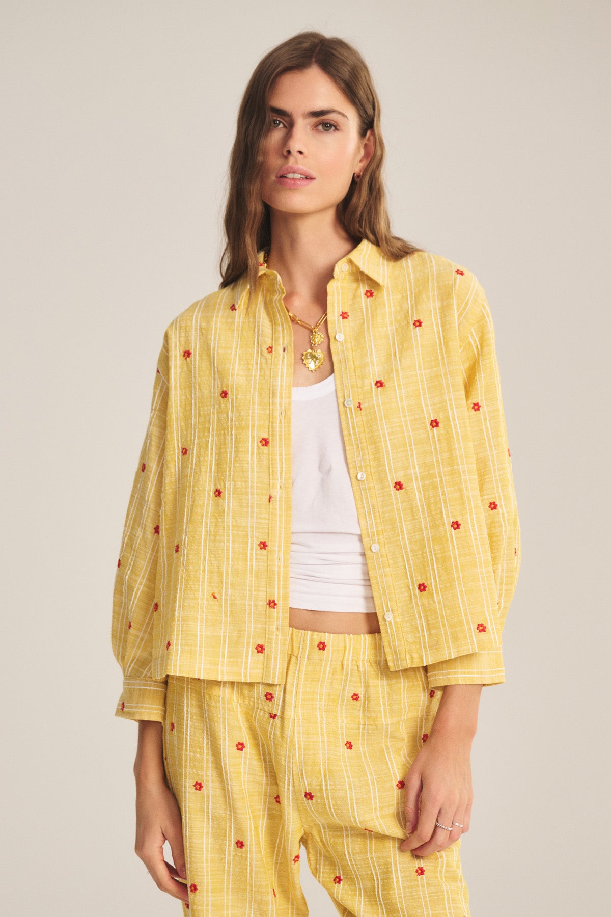 A woman wears the ASTREN SHIRT by Velvet by Graham & Spencer, a yellow plaid cropped top with red accents, layered over a white tank, set against a plain background.