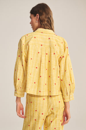 A woman is seen from the back wearing the ASTREN SHIRT by Velvet by Graham & Spencer, a yellow cropped long-sleeve top with matching pants featuring red dots and vertical white stripes.