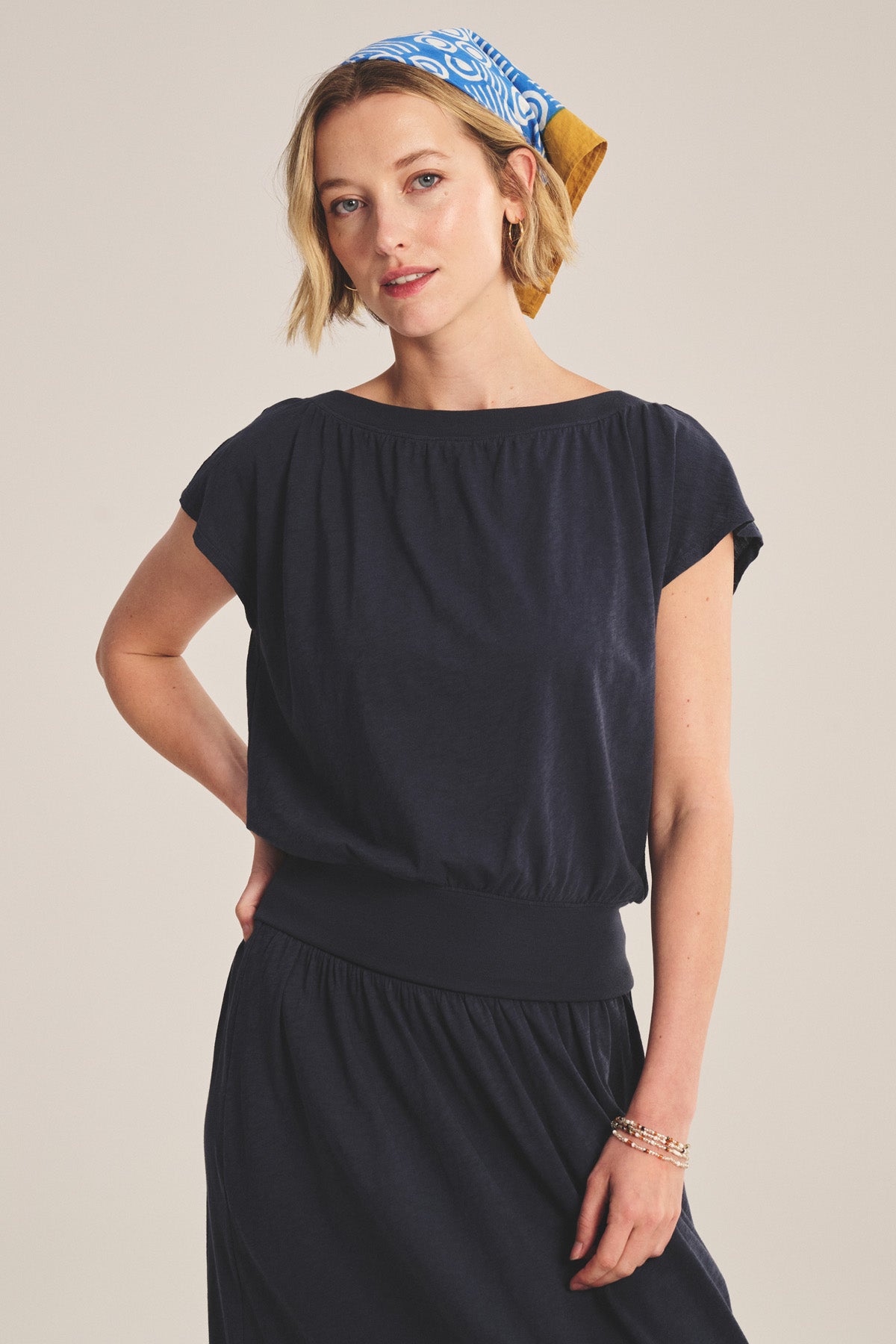 A woman wears the AUDEN TEE by Velvet by Graham & Spencer, styled with a blue patterned headscarf and standing against a plain background.