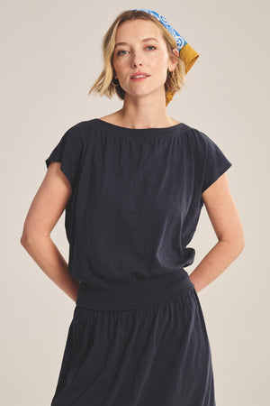 Woman wearing the AUDEN TEE by Velvet by Graham & Spencer, styled for everyday wear with a patterned headscarf, standing with hands behind her back against a plain background.
