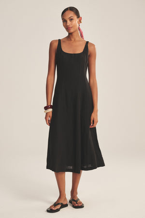 A woman faces forward wearing the AUSTEN LINEN DRESS by Velvet by Graham & Spencer, styled with black sandals, a red hair scarf, and bracelets, set against a plain light background.