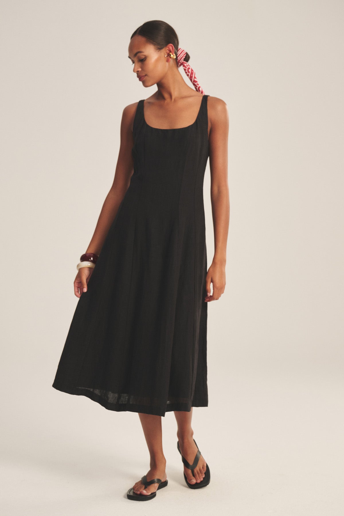 A woman in the AUSTEN LINEN DRESS by Velvet by Graham & Spencer, styled with black sandals and a red patterned hair scarf, stands against a plain light background.