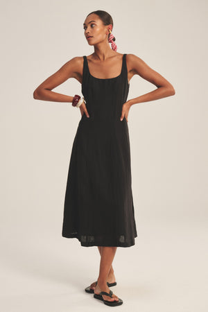 A woman wears the AUSTEN LINEN DRESS by Velvet by Graham & Spencer with black sandals, a red hair scarf, and a bracelet, set against a plain light background.