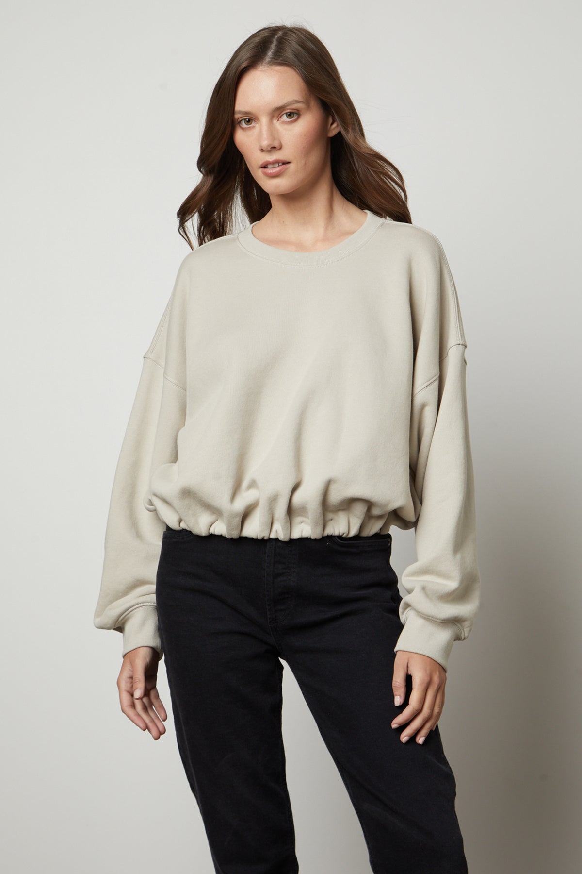   The versatile model is wearing a Velvet by Graham & Spencer BOBBI CROPPED SWEATSHIRT in a beige color and black jeans. 