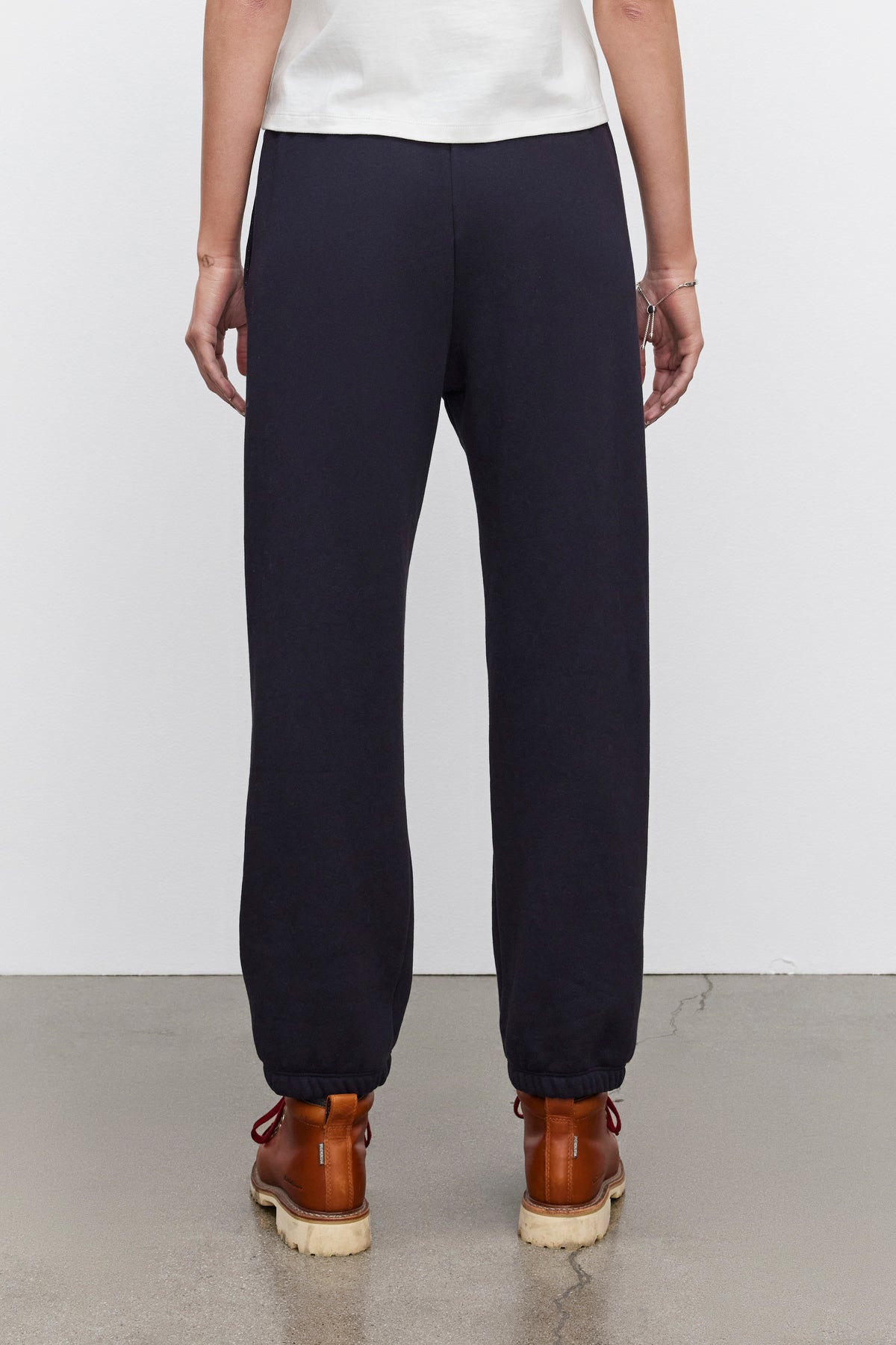   A person is wearing Velvet by Graham & Spencer CELESTA SWEATPANT and brown boots, standing on a concrete floor with their back facing the camera, exuding warmth and comfort. 