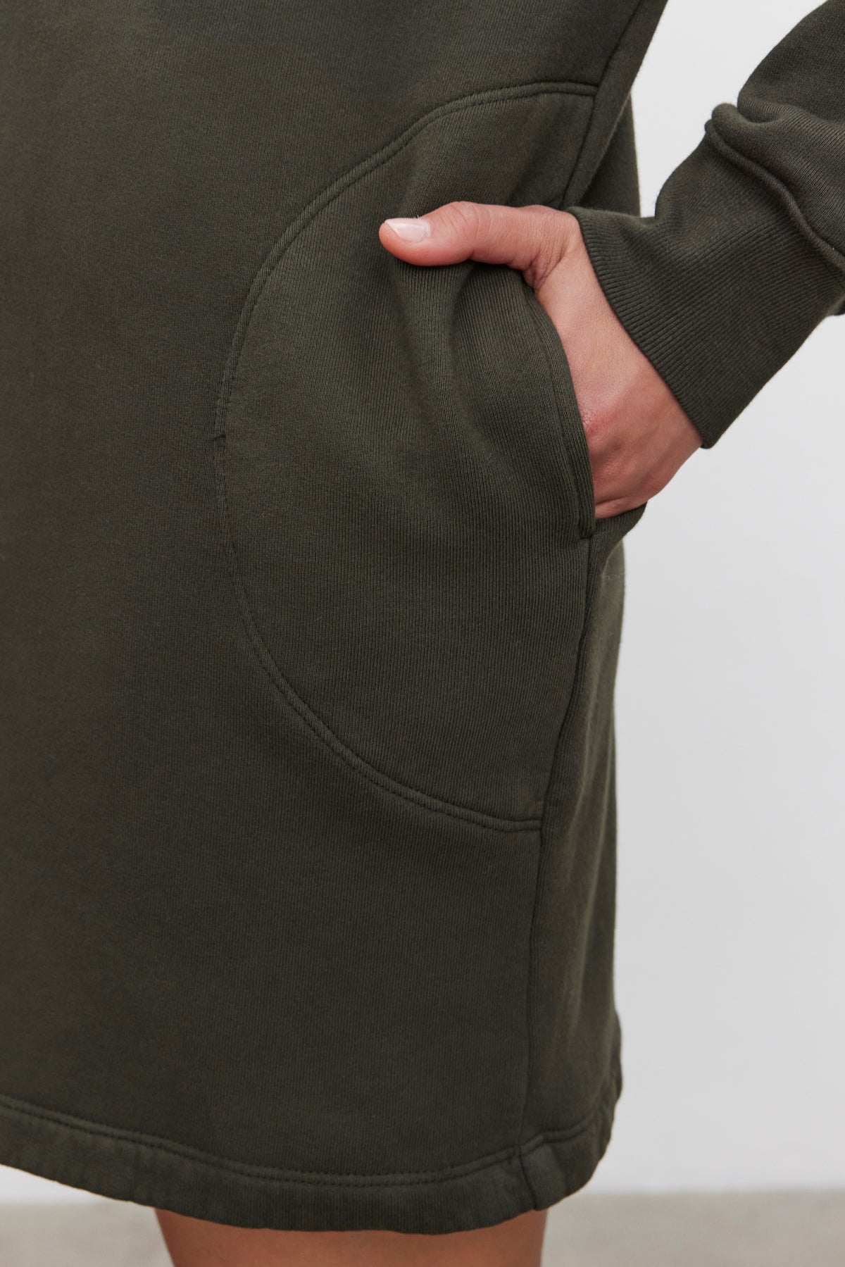   Close-up of a hand partially inserted into the pocket of a long-sleeved, dark green ETTA HOODIE DRESS in cotton fleece by Velvet by Graham & Spencer. 