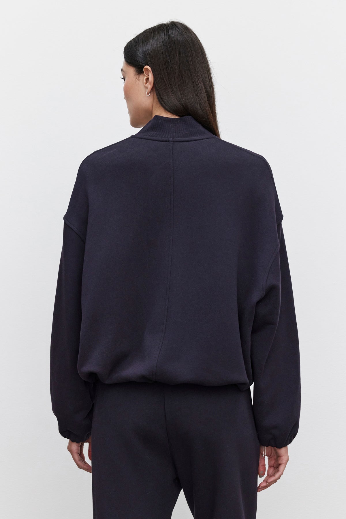   Rear view of a person wearing an oversized fit, long-sleeved GENEVIEVE ZIP-UP SWEATSHIRT by Velvet by Graham & Spencer and matching pants. The sweatshirt is made of heavier-weight cotton fleece. The person has long, dark hair. 