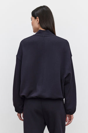 Rear view of a person wearing an oversized fit, long-sleeved GENEVIEVE ZIP-UP SWEATSHIRT by Velvet by Graham & Spencer and matching pants. The sweatshirt is made of heavier-weight cotton fleece. The person has long, dark hair.