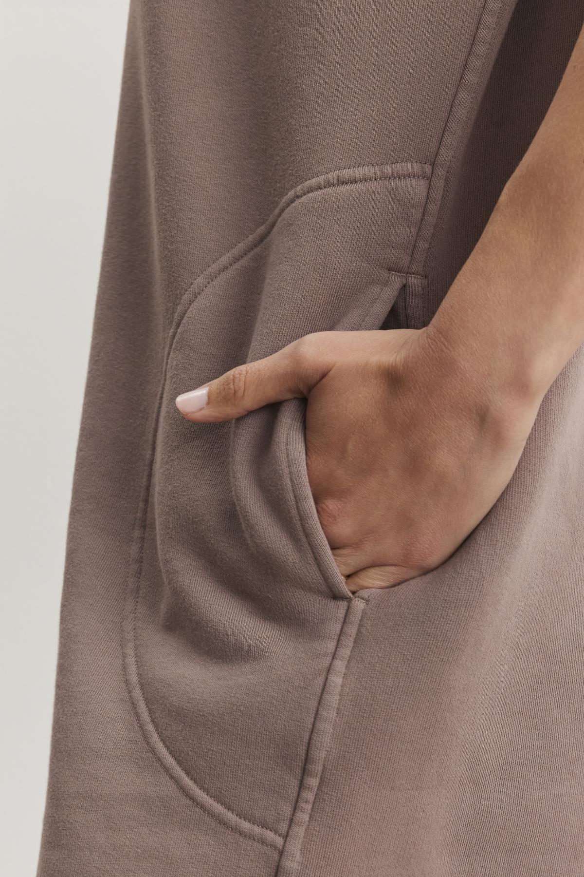 Close-up of a hand in the pocket of the LITTA DRESS by Velvet by Graham & Spencer, highlighting its sweatshirt style in brown cotton fleece.-38483614335169